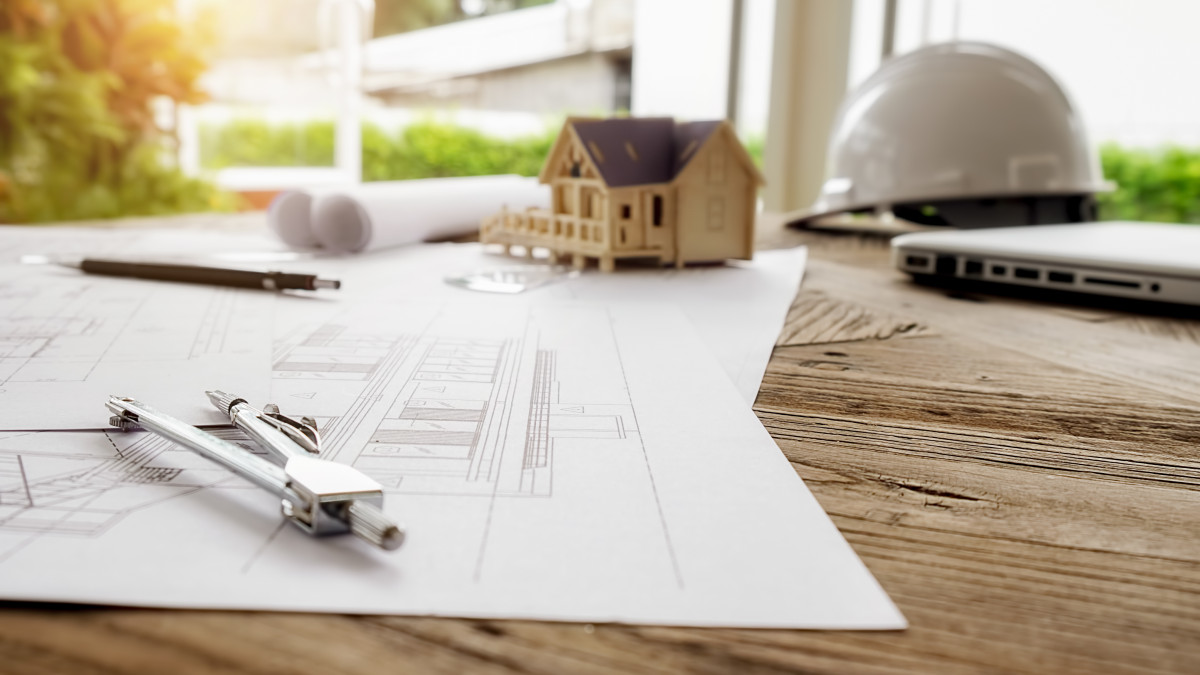 le bureau d'un constructeur de maison avec un plan, un casque, un compas, un stylo et la miniature d'une maison